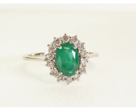 18CT WHITE GOLD, EMERALD AND DIAMOND CLUSTER RING, the four claw set oval emerald with a surround of fourteen melee diamonds,