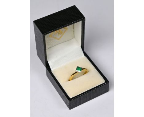 An emerald set single stone ring, the square cut collet set emerald set off centre on 18ct yellow gold knife-edge shank, size