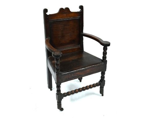 A late 17th/18th century oak chair, with panel back over shaped arms, two plank seat and bobbin turned front stretcher