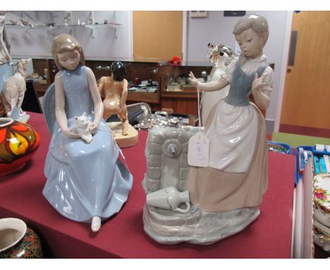 A Nao Figure of a Girl, with a cat on her lap; together with a Nao figure of a girl by a well.