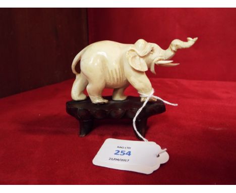 A carved ivory elephant resting on a wooden base     Trunk has bee off and re-glued and tusk