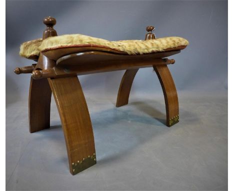 A 20th century camel stool, with wild cat skin and camel hide cushion, on stud bound bowed legs, H.43 W.68 D.36cm 