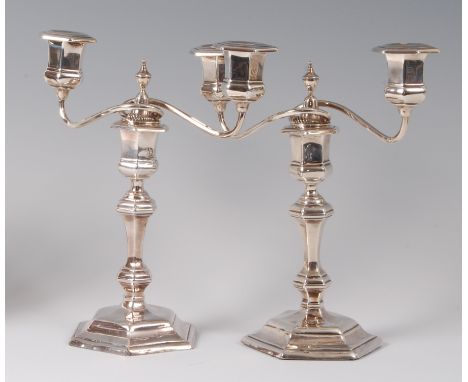 A pair of silver two-light candelabra, each in the Queen Anne style, having multi-knopped columns to loaded hexagonal bases, 