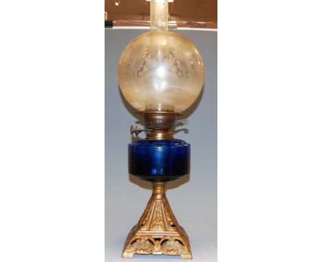 An early 20th century oil lamp, having etched globular clear glass shade to a blue glass font, on pierced iron base