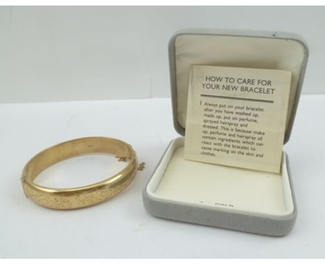 A 9CT GOLD BANGLE of hinged form, the clasp with safety chain, one half is plain, the other with chased floral decoration, 14