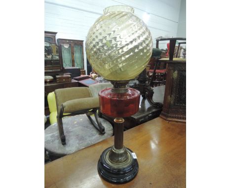 A late Victorian/Edwardian oil lamp having wrythen amber colour globe on ruby glass reservoir and brassed column 