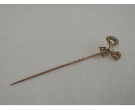 A yellow metal stick pin having bow detail with seed pearl decoration, no marks, tested as 9ct gold