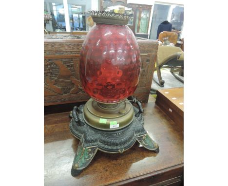 A 20th century oil lamp having dimpled cranberry glass shade on brass and cast metal base