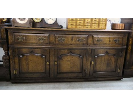 A modern reproduction of an Old English style, stained oak dresser with three in-line drawers, over three panelled doors, rai