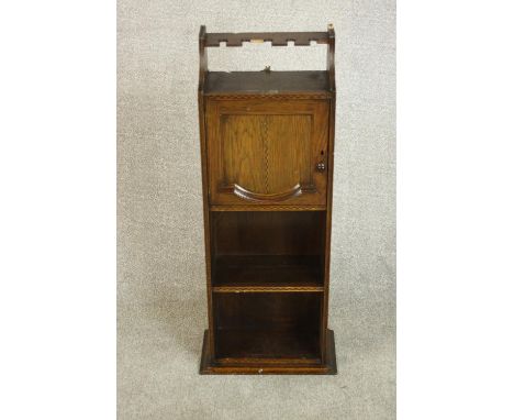 An early 20th century oak drinks cabinet, with a glasses rack over a cupboard door above shelves. H.90 W.30 D.19cm. 