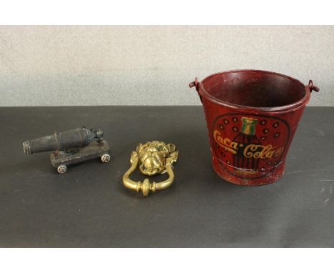 A large brass lion head door knocker along with a painted iron bucket with a coca cola design and an iron canon. H.20 Dia.24c