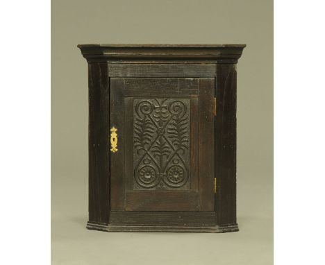 A small oak hanging corner cupboard, with carved panelled door opening to a shaped shelf.  Height 58 cm, width 51 cm, depth 3