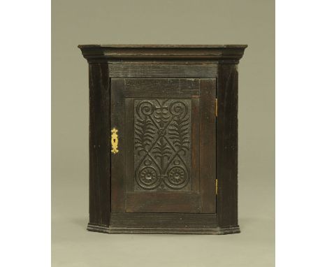 A small oak hanging corner cupboard, with carved panelled door opening to a shaped shelf.  Height 58 cm, width 51 cm, depth 3