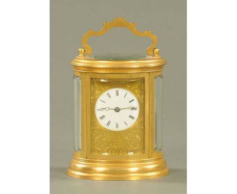 An Edwardian oval brass carriage clock, foliate engraved and with two train movement striking on a bell, height excluding car