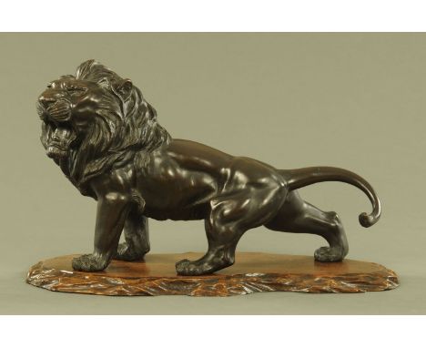 A large Chinese bronze prowling lion, with rectangular seal mark beneath and raised on a wooden plinth.  Length 58 cm, height