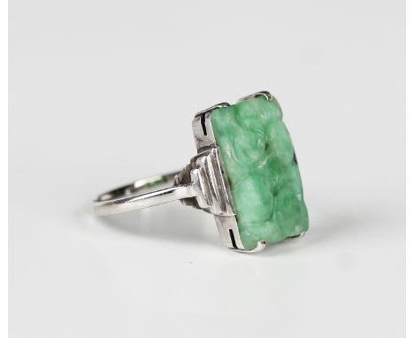 A white gold and jade ring, mounted with a rectangular jade with carved and pierced decoration between stepped shoulders, det