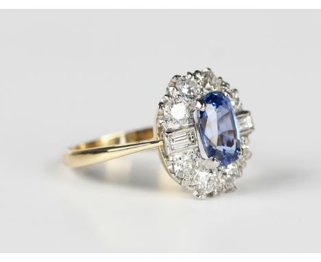 A gold and platinum, sapphire and diamond cluster ring, claw set with the oval cut sapphire within a surround of eight circul