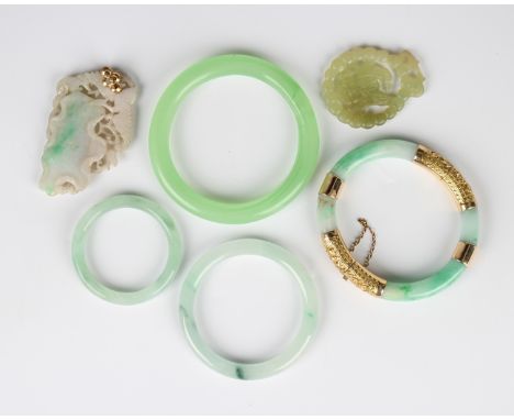A Chinese gold mounted jade oval hinged bangle, the mounts decorated with dragons, fitted with a safety chain, unmarked, insi