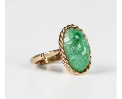 A gold and jade ring, the oval jade with carved decoration within a ribbon twist surround, detailed '9ct', weight 5.4g, ring 