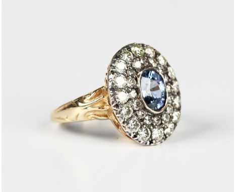 A gold, sapphire and diamond cluster ring, collet set with the oval cut sapphire within a twin surround of circular cut diamo