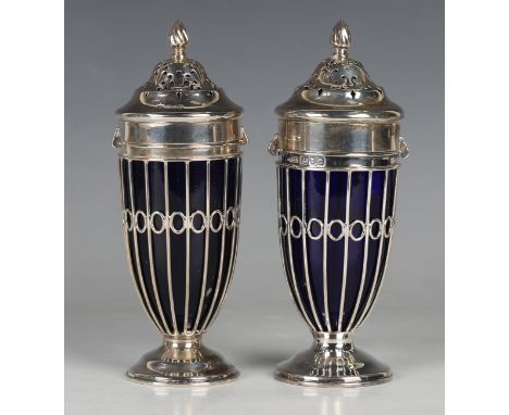A near pair of silver sugar casters, each pierced cover with flame finial above a pierced wirework body and blue glass liner,
