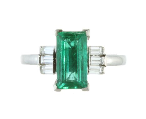 AN EMERALD AND DIAMOND DRESS RING in platinum, set with a step cut emerald of 1.85 carats between trios of baguette cut diamo