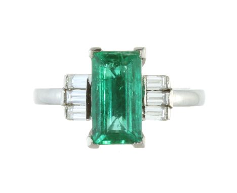 AN EMERALD AND DIAMOND DRESS RING in platinum, set with a step cut emerald of 1.85 carats between trios of baguette cut diamo