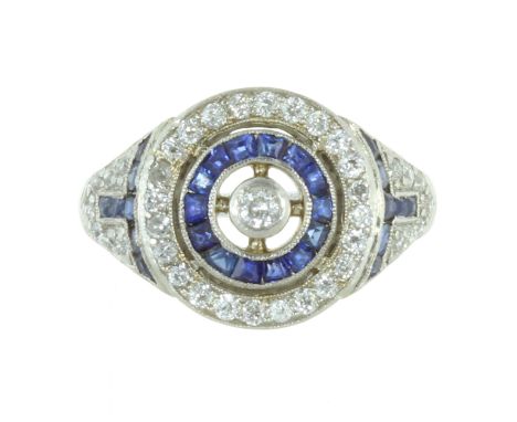 AN ART DECO DIAMOND AND SAPPHIRE DRESS RING in white gold or platinum, set with a central round cut diamond, encircled by con