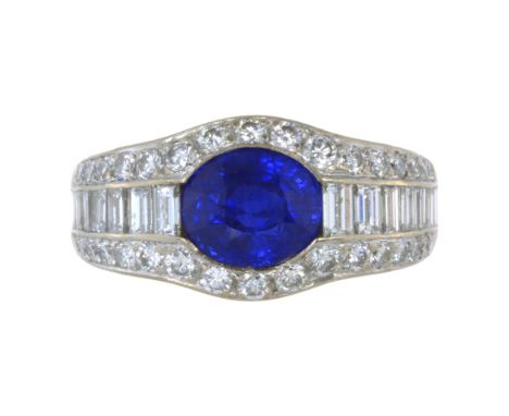 A BLUE SAPPHIRE AND DIAMOND DRESS RING in platinum, set with a central oval cut blue sapphire of 3.05 carats between two rows