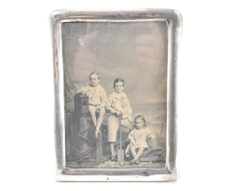 A hallmarked silver fronted picture frame. The frame having a plain exterior face with rounded edges to the top. Easel backed