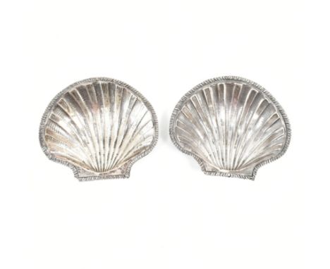 A pair of silver scallop shell salt dishes. The shallow bowls both in the form of repousse scallop shells with feather gadroo