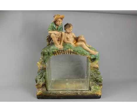 A vintage glass fish tank; standing on a composite support depicting two young boys admiring the tank from a bridge, the tank