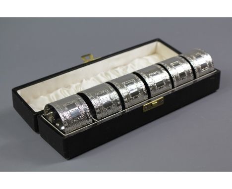 Cased set of six silver circular napkin rings; engine turned with floral engraved borders, housed in the original presentatio