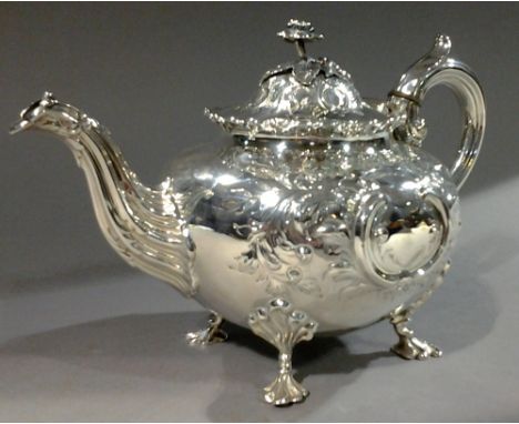 A silver teapot
The body with embossed scrolling leaf, the hinged cover with rose finial, standing on flattened scroll feet. 