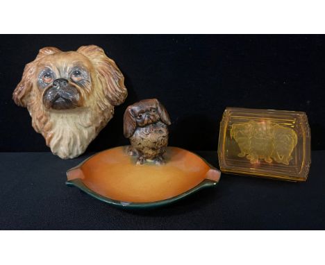 Pekingese Interest - a ceramic wall mask, 15.5cm wide;  a German ash tray, surmounted with Pekinese, 16cm wide;  an amber gla