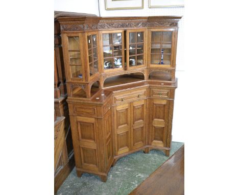 An oak corner cabinet, outswept cornice, floral carving to frieze, four astragal glazed doors enclosing shelving over recesse