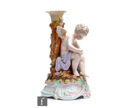 An early 20th Century Dresden type candlestick modelled as a seated cherub restringing a bow with a quiver of arrows beneath 