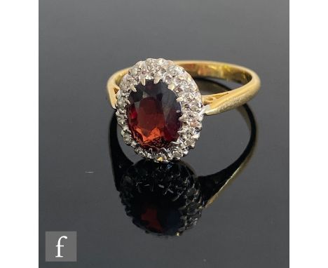 An 18ct garnet and diamond cluster ring, central oval garnet within a border of diamonds, all to knife edged shoulders, weigh
