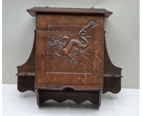 A 20TH CENTURY CRAFTSMAN BUILT OAK HANGING CUPBOARD with carved dragon panelled single door, the unit flanked by twin candle 