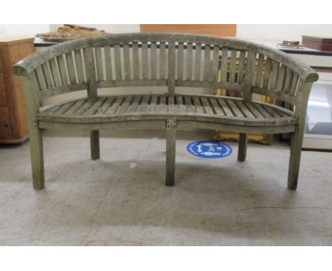 A modern teak garden bench of curved slatted design, raised on block legs&nbsp; 66"w&nbsp; 