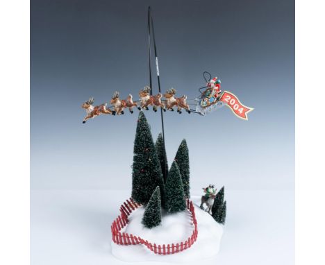 A snowy hillside, framed by decorated pine trees and a red picket fence, features an elf on a reindeer peering through binocu