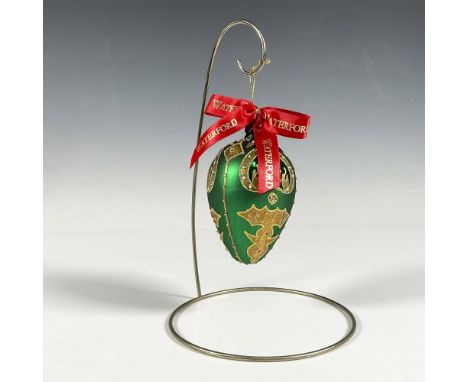Handcrafted ornament adorned with gold decorative elements that include holly leaves and a stylized fleur de lis crown. The s