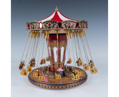 This whimsical centerpiece showcases tiny figures joyfully swinging around on a carousel, accompanied by twinkling lights and
