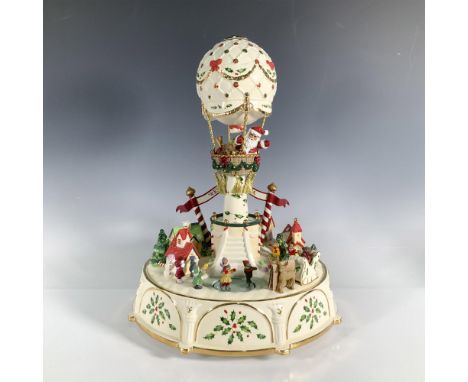 A festive winter scene is centered around Santa waving from a hot air balloon. Holly and berries decorate the sides of the ce