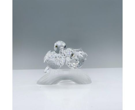 Two clear crystal turtledoves cuddle each other while perched atop a frosted branch, their melon-colored eyes gleaming. Swaro