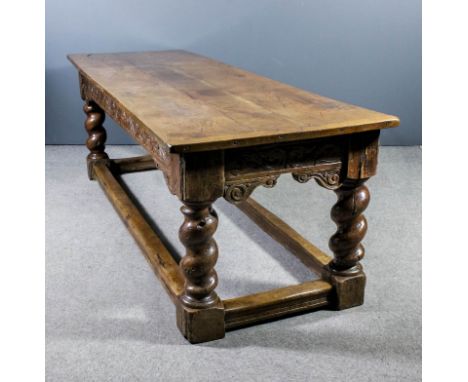 An old oak refectory table of "17th Century" design with cleated three plank top, the frieze carved with scroll ornament, on 