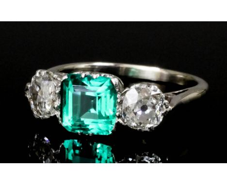 A modern silvery coloured metal mounted emerald and diamond three stone ring, the central square cut emerald 1.22ct shouldere