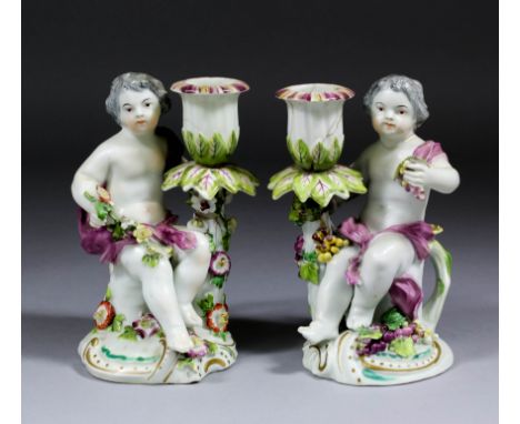 A pair of 18th Century Derby porcelain figural candlesticks (circa 1765) modelled with seated putti supporting candle sconces