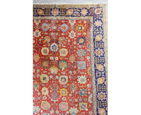 A Kirman carpet woven in colours with bold floral palmettes and a central urn on a terracotta ground and within floral filled