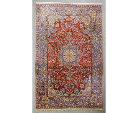 An Isfahan carpet woven in colours with a bold central medallion, palmettes and leaf scroll ornament on a brick red ground wi